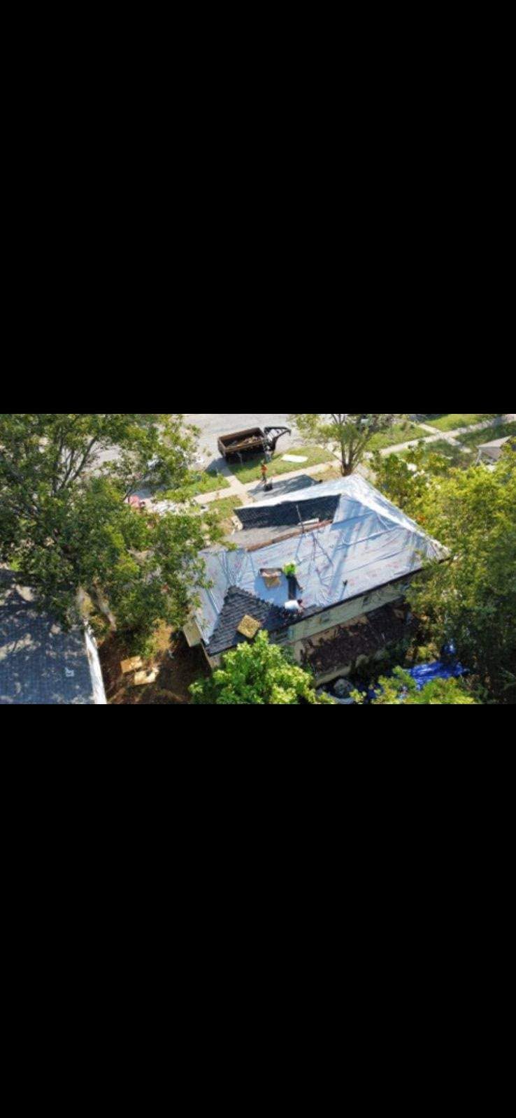Roofers work on a tarp-covered house with a dumpster nearby.