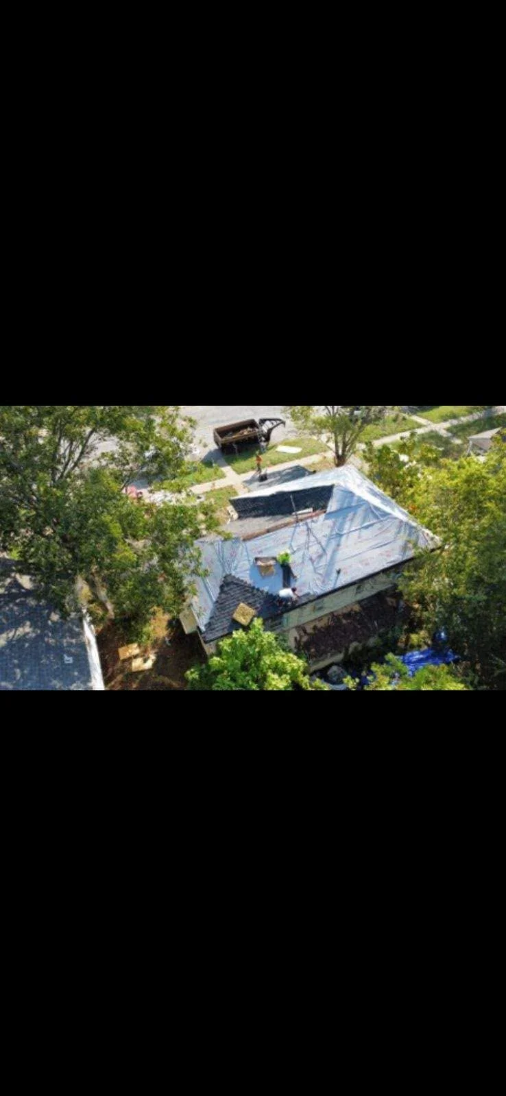 Roofers work on a tarp-covered house with a dumpster nearby.