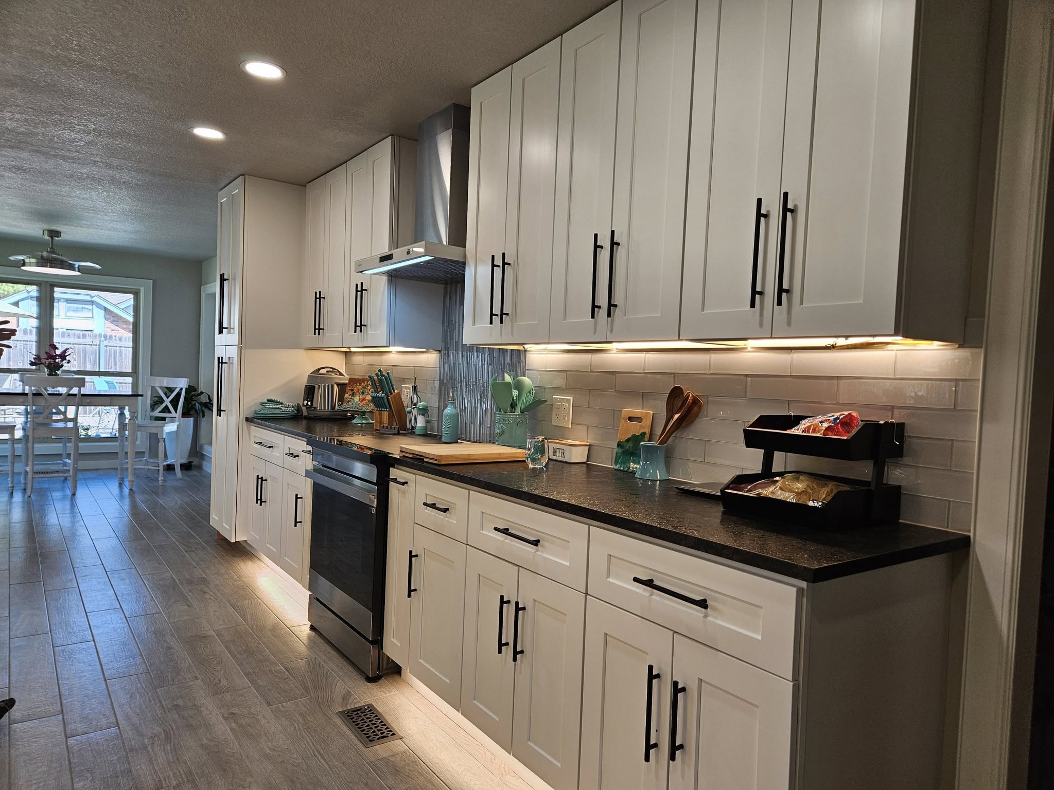 A modern white kitchen with dark countertops and stainless steel appliances.