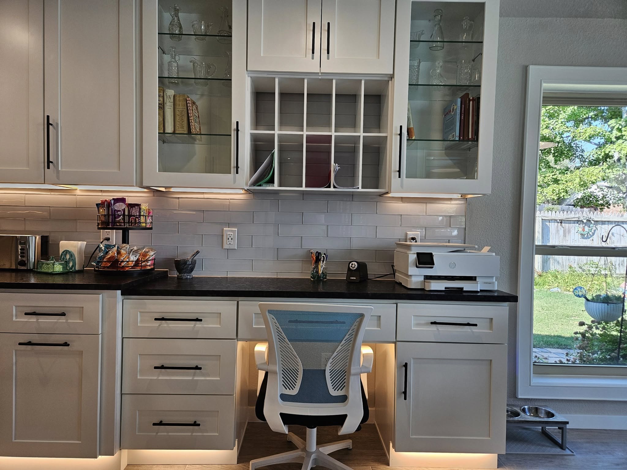 A home office setup with a desk, chair, printer, and cabinets in a kitchen.