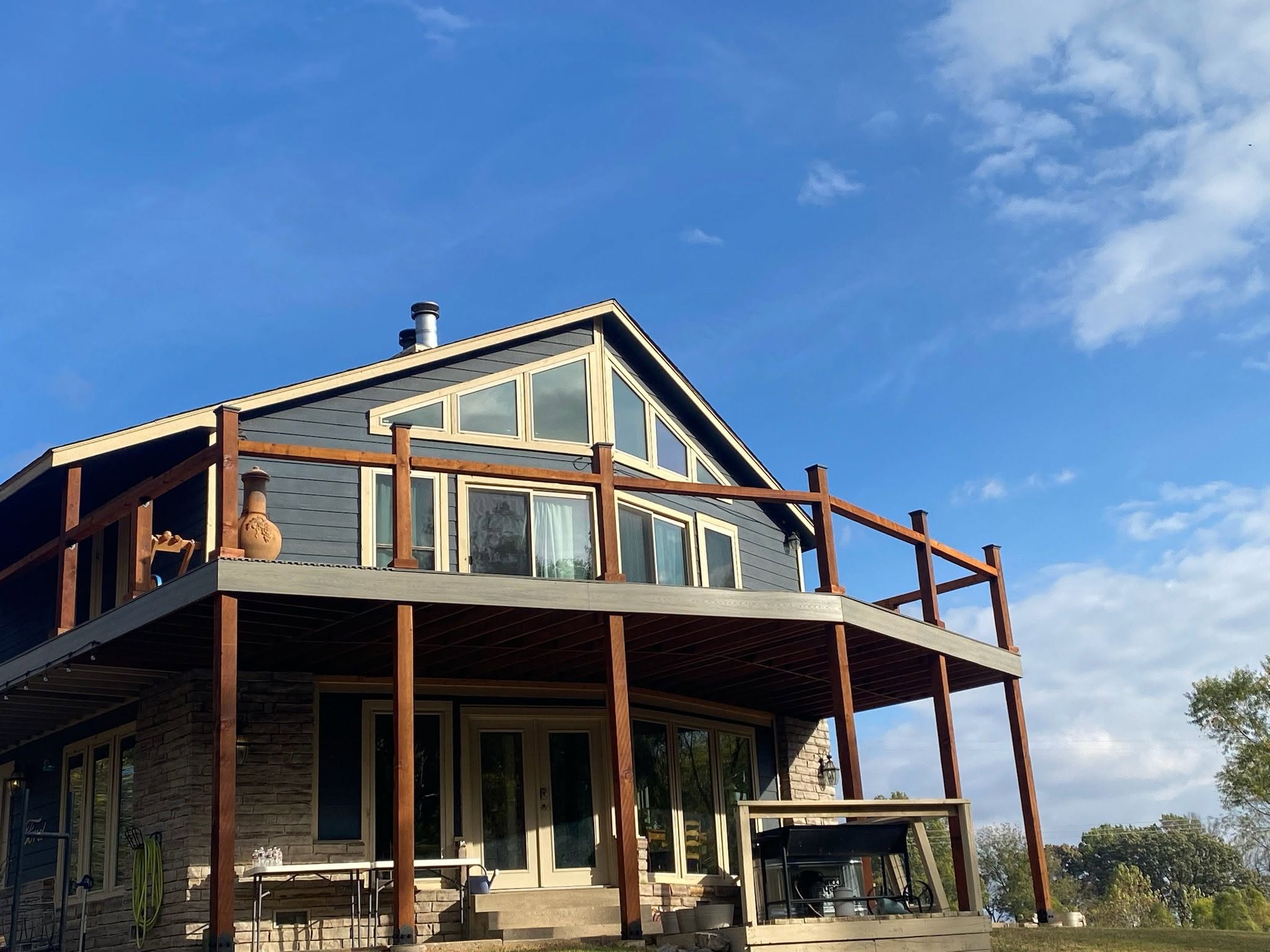 A modern house with a large deck under a blue sky with clouds.