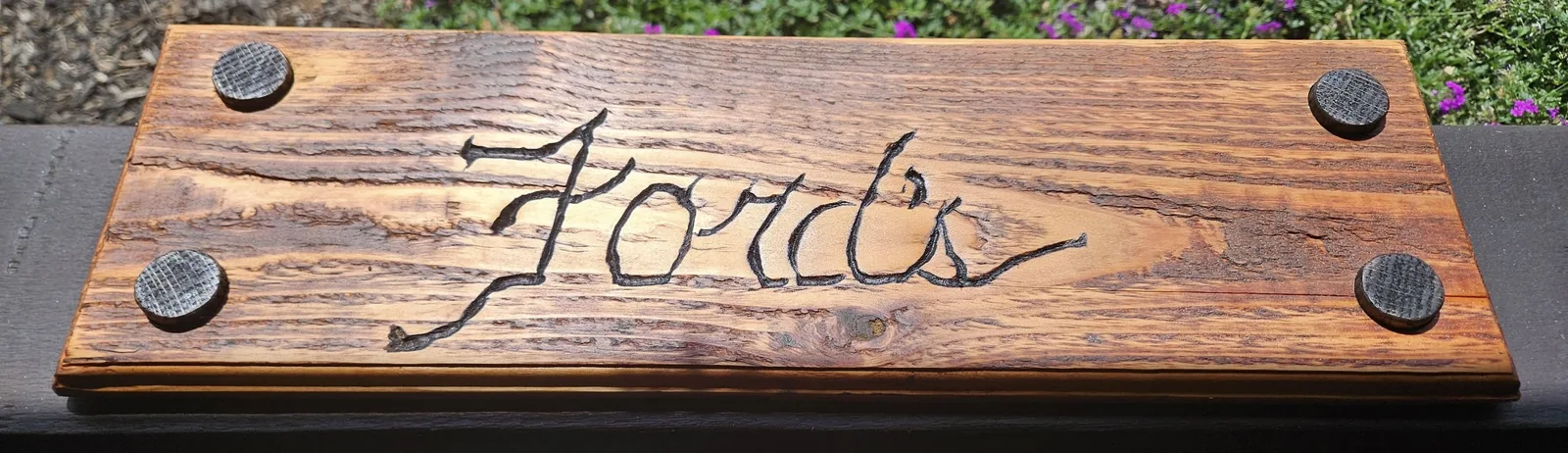 A wooden sign with "Ford's" carved into it, mounted with four circular fasteners.