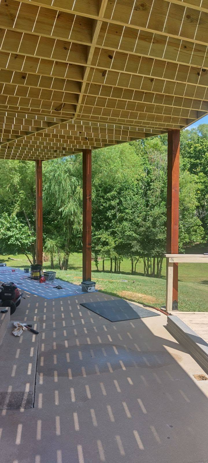 A wooden deck is under construction over a concrete patio with trees in the background.