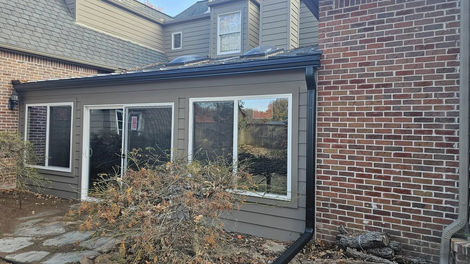 A house addition with large windows and a brick wall is shown outdoors.
