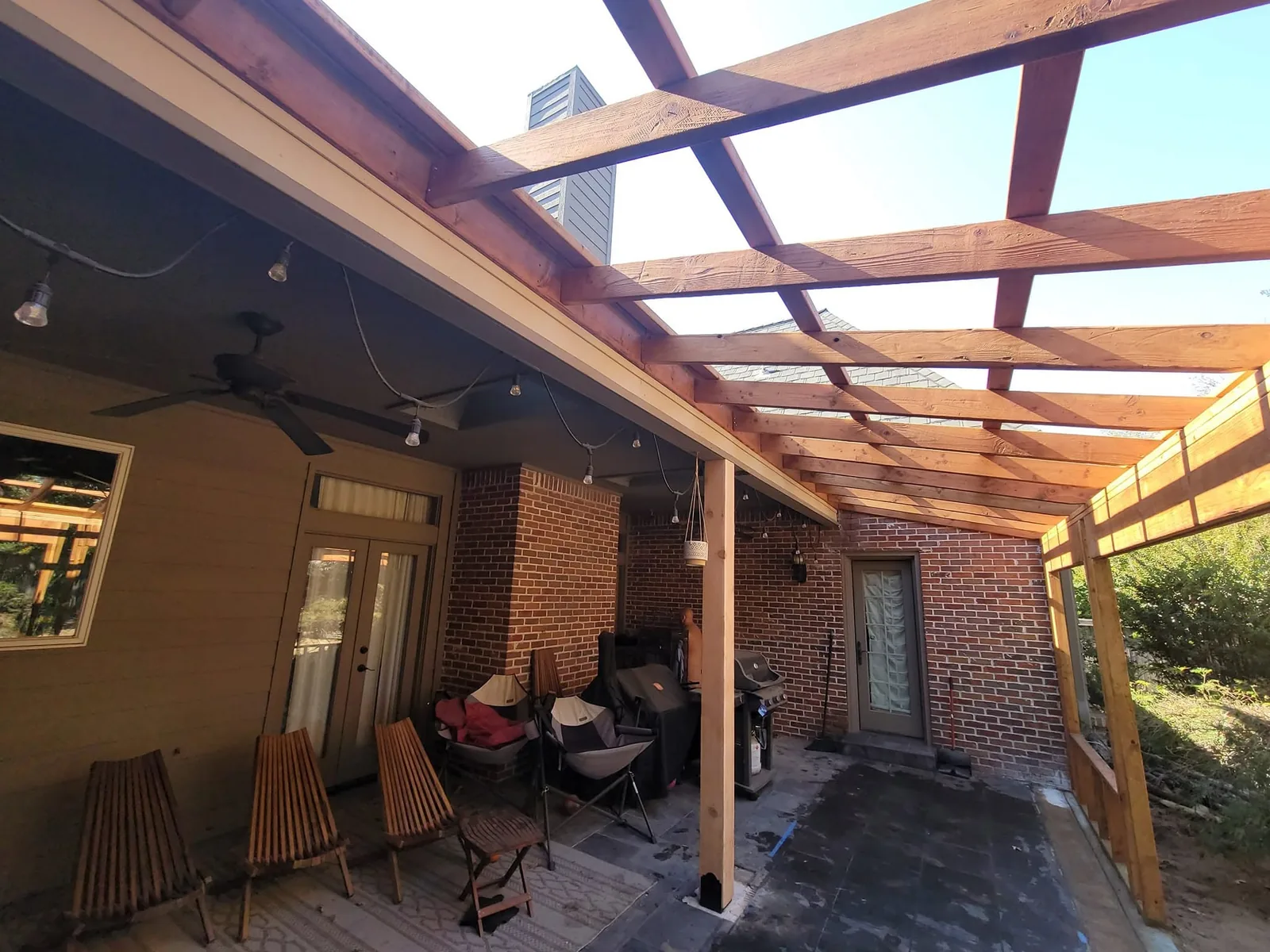 An outdoor patio with a wooden pergola, furniture, and a grill.